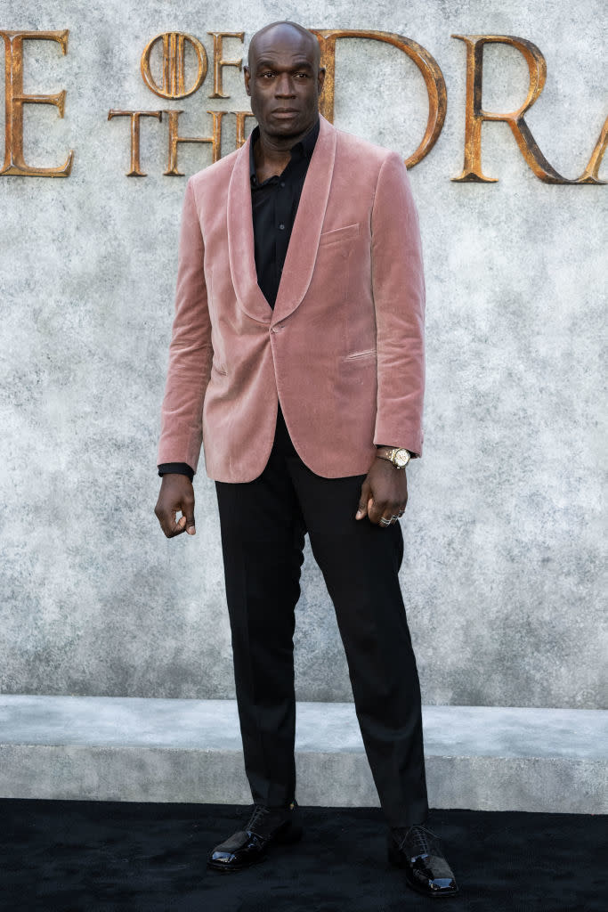 House of the Dragon event: A person in a pink velvet blazer, black shirt, and black pants stands in front of a textured backdrop with large text partially visible