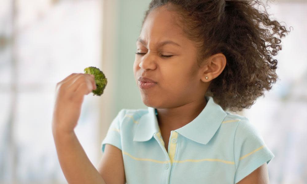 A child grimacing towards some broccoli