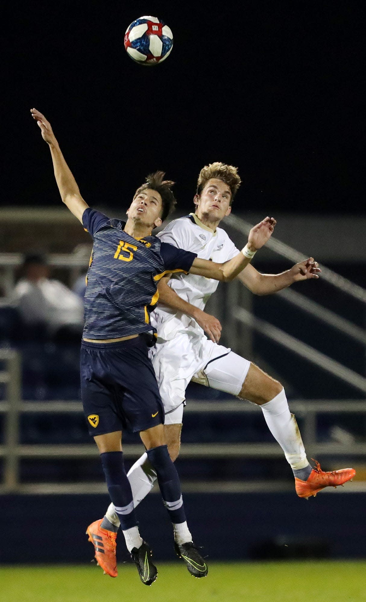 Akron Zips midfielder Sam Tojaga, right, heads the ball against West Virginia forward Tony Pineda (15) during the first overtime period of an NCAA soccer game, Wednesday, April 7, 2021, in Akron, Ohio. [Jeff Lange/Beacon Journal]