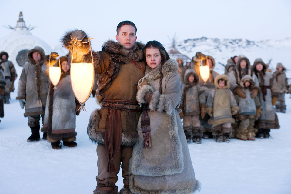 couple standing in the cold with a lantern while a group of people stand behind them