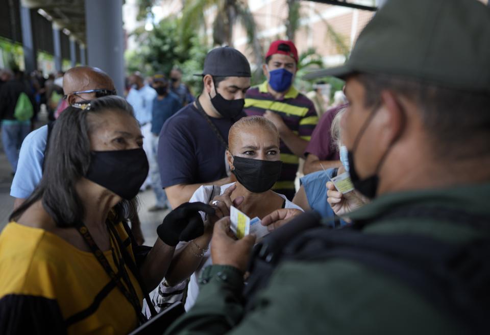 A Bolivarian National Guard checks a residents' vaccination cards as they wait to be injected with a second dose of the Sputnik V COVID-19 vaccine after more than a three-month delay, in Caracas, Venezuela, Tuesday, Sept. 21, 2021. (AP Photo/Ariana Cubillos)