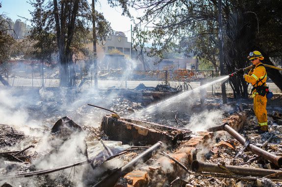 A firefighter sprays the remains of a house destroyed by a wildfire in Lower Lake, California, Aug. 15, 2016.