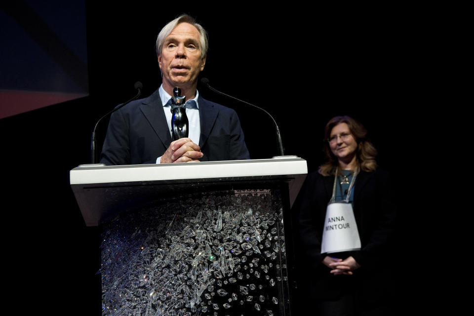 This June 4, 2012 photo shows fashion designer Tommy Hilfiger accepting his award during a rehearsal for the CFDA Awards in New York as an unidentified woman stands in for Vogue editor Anna Wintour, who later presented the award. Hilfiger has been in the fashion business for more than 40 years, starting at a little denim shop in Elmira, N.Y., and now at the helm of a brand that's one of the most recognizable in the world. This spring, he added “American Idol” style adviser to his resume. His peers at the Council of Fashion Designers of America honored him Monday night with a lifetime achievement award. (AP Photo/Charles Sykes)