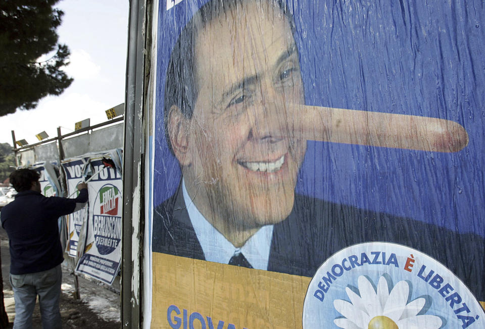 FILE - A man sticks posters of Forza Italia party (Go Italy) reading, Vote Berlusconi President, background left, as an electoral posters by The Daisy party of the center-left coalition bearing the mock pictures of Italian Premier Silvio Berlusconi is seen in Rome, on April 7, 2006. Berlusconi, the boastful billionaire media mogul who was Italy's longest-serving premier despite scandals over his sex-fueled parties and allegations of corruption, died, according to Italian media. He was 86. (AP Photo/Gregorio Borgia, File)