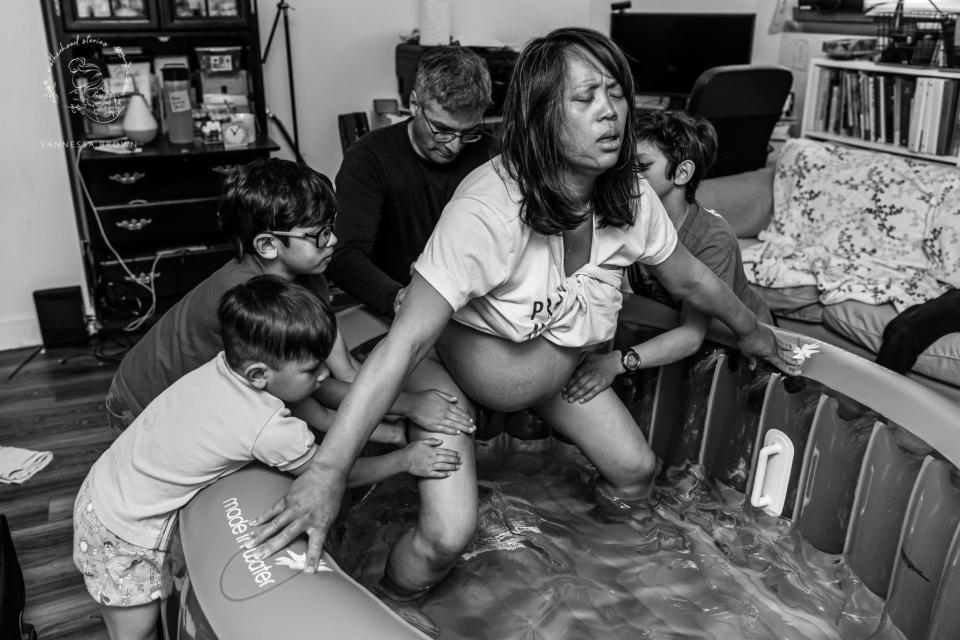 Three boys and a father touch their mother supportively as she labors