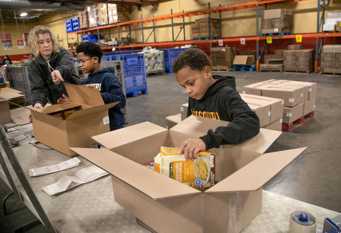 Adriane New and her sons Babriel, 12, and TJ, 10, box groceries during a Harvesters volunteer event Monday.