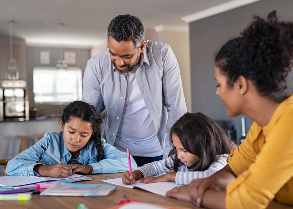 A couple help their two children with their studies, seated at dining room table