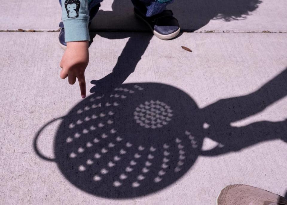 Wally Harrell, 3, looks at the crescent-shaped shadow of the solar eclipse as his mother Caroline holds a colander at Museum of Science and Curiosity in Sacramento on Monday, April 8, 2024. Paul Kitagaki Jr./pkitagaki@sacbee.com