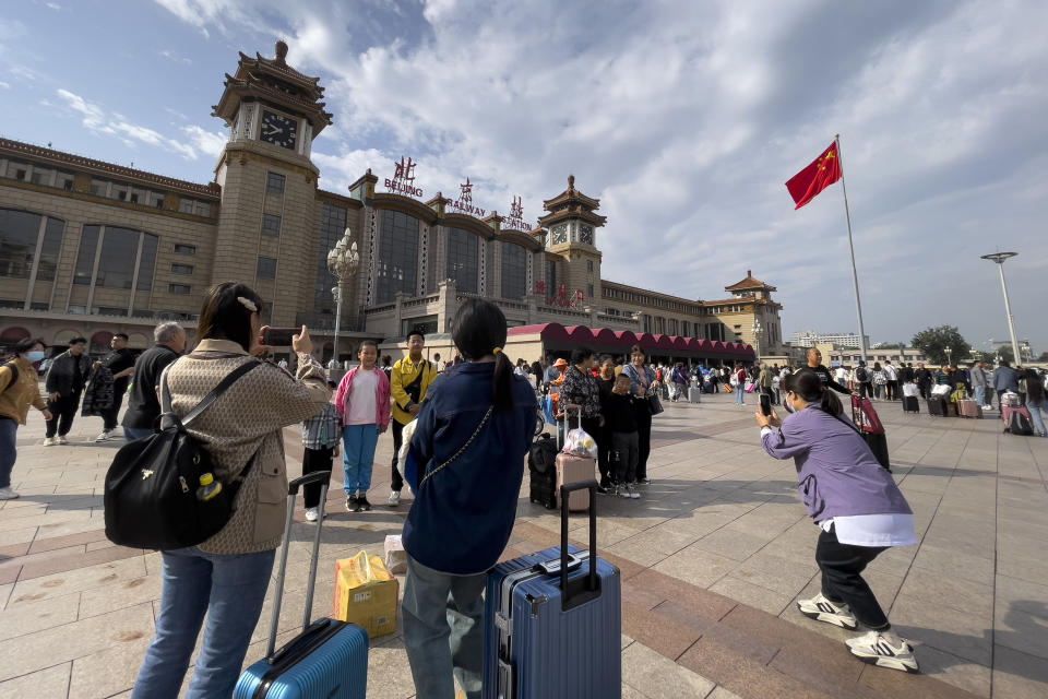 Travelers take souvenir photos as they arrive at Beijing Railway Station in Beijing, Friday, Sept. 29, 2023. Tens of millions of Chinese tourists are expected to travel within their country, splurging on hotels, tours, attractions and meals in a boost to the economy during the 8-day autumn holiday period that began Friday. (AP Photo/Andy Wong)