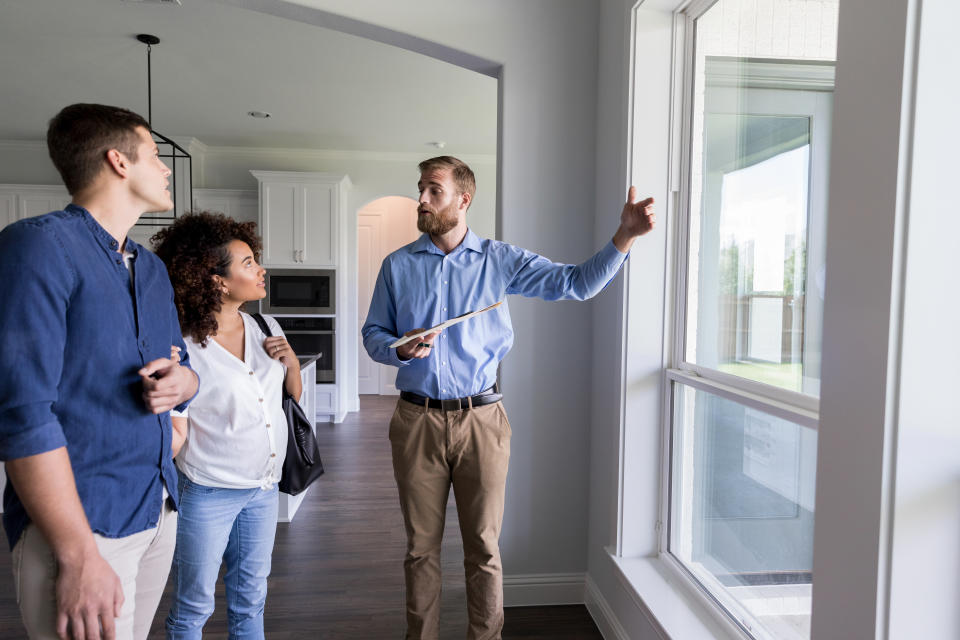 Confident male Real Estate Agent shows potential homeowners a view from the living room windows in the home.