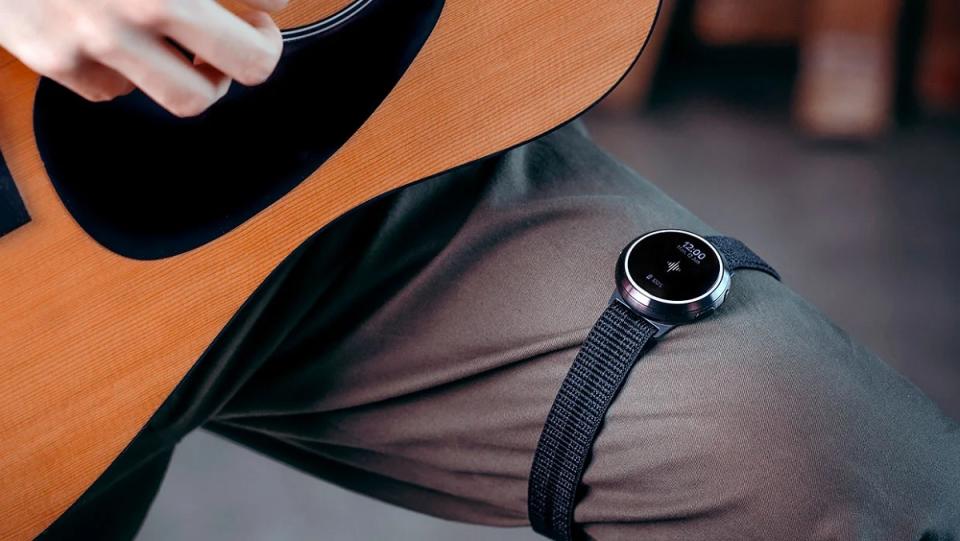 A Soundbrenner Smartwatch sits on the knee of a guitar player.