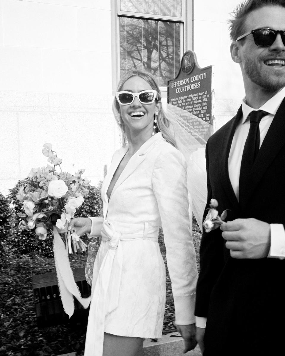A black-and-white photo of a bride and groom smiling and walking together.