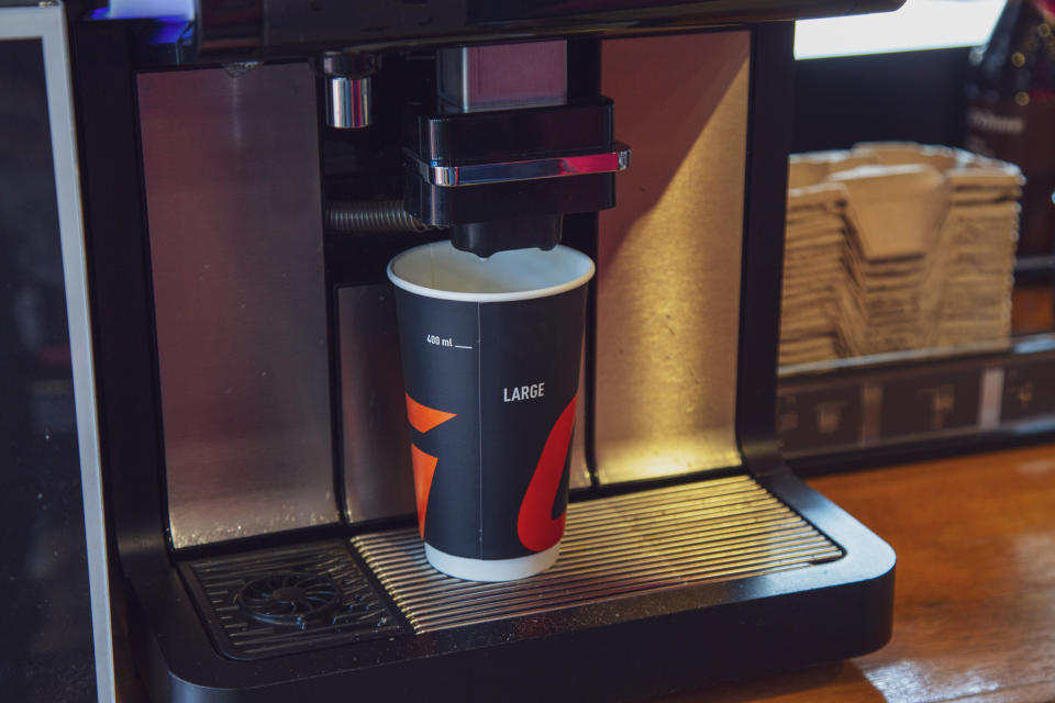 A large coffee machine dispenses a drink into a cup labeled "Large." Nearby, napkins are stacked in a holder