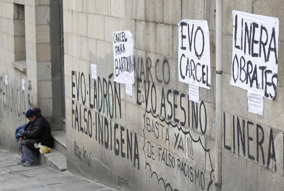 A woman rests at the entrance of a building whose walls are covered with graffiti agains Bolivia's former President Evo Morales, in La Paz, Bolivia, Monday, Nov. 11, 2019. Morales' Nov. 10 resignation, under mounting pressure from the military and the public after his disputed re-election victory triggered weeks of fraud allegations and deadly demonstrations, leaves a power vacuum and a country torn by protests against and for his government. (AP Photo/Juan Karita)