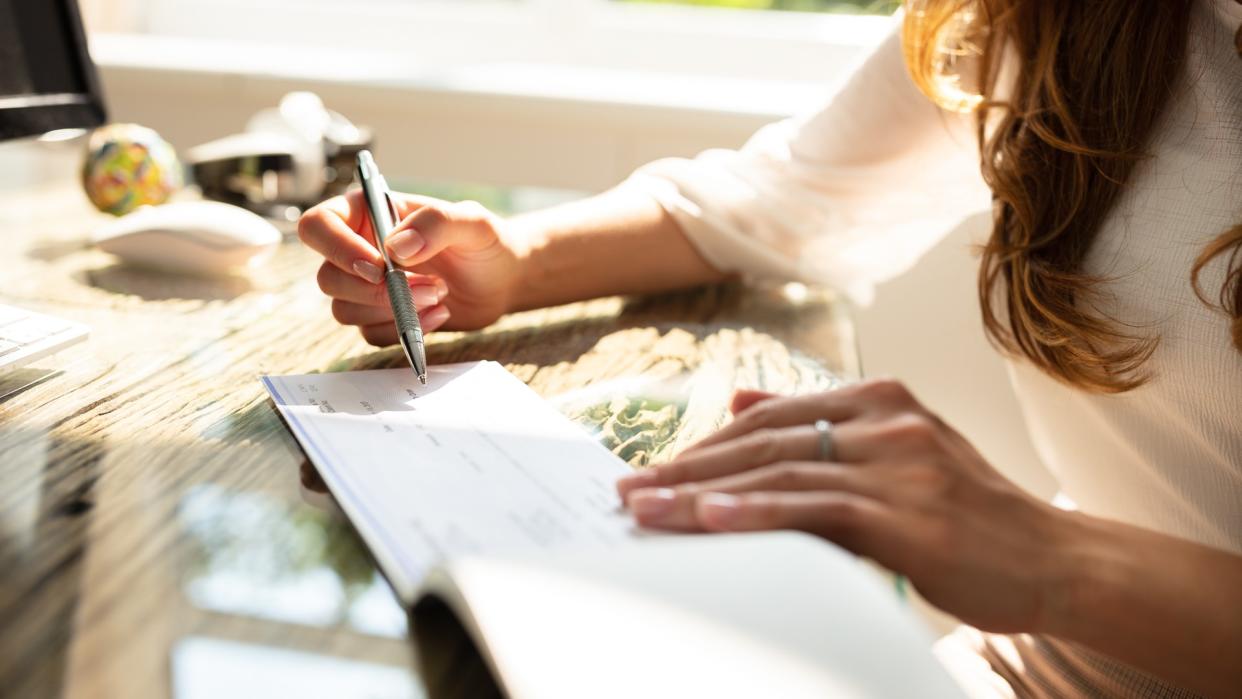 Businesswoman's Hand Signing Cheque On Wooden Desk.