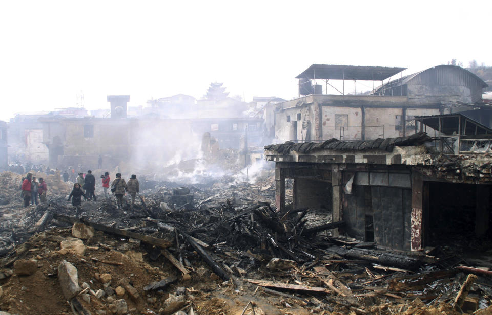 In this Sunday, Jan. 12, 2014 photo, people walk over debris of burnt houses in the ancient town of Dukezong after a fire broke out on last Saturday, in Shangri-la county in southwest China's Yunnan province. A fire prevention system costing more than $1 million wasn't functioning and failed to prevent a blaze that razed an ancient tourist town in southwest China, the fire service said Monday. (AP Photo) CHINA OUT