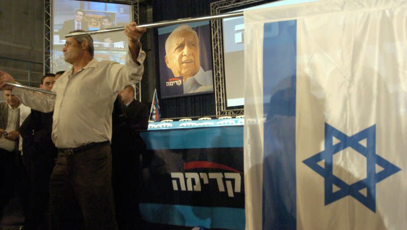 An Israeli man waves an Israeli flag in front of a poster of Kadima founder Prime Minister Ariel Sharon at the Kadima victory celebration in Neve Ilan, March 29, 2006. On April 11, 2006, Sharon was officially relieved of his duties as prime minister of Israel when the Cabinet declared him to be permanently incapacitated. Sharon had a major stroke on Jan. 4, 2006, and fell into a coma a short time later. File Photo by Debbie Hill/UPI