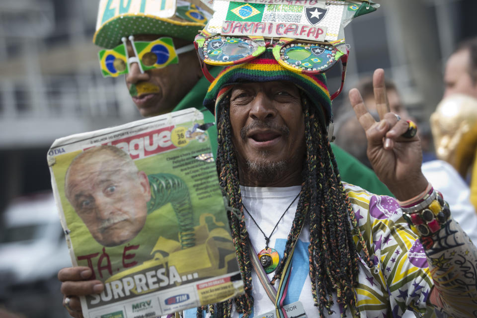 A Brazil soccer fan holds up a newspaper with a photo of Brazil's coach Luiz Felipe Scolari and flashes a victory sign outside the venue where coach Luiz Felipe Scolari is announcing his squad for the upcoming international soccer tournament in Rio de Janeiro, Brazil, Wednesday, May 7, 2014. The team will mix talented young stars such as Neymar and Oscar with more experienced players such as Dani Alves, David Luiz, Thiago Silva and Hulk. Past stars such as Ronaldinho, Kaka and Robinho were left off the squad as expected. (AP Photo/Silvia Izquierdo)
