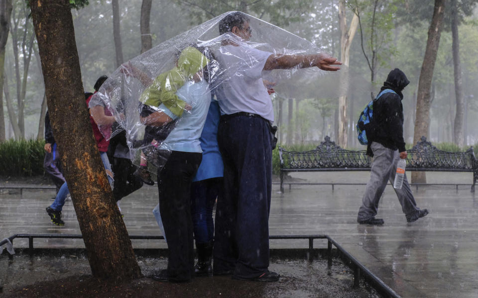 In this Aug. 12, 2018 photo, Fernando Rodriguez Garcia covers his family with a plastic sheet during a sudden downpour as he and his family take a walk through Alameda park in Mexico City. (AP Photo/Anthony Vazquez)