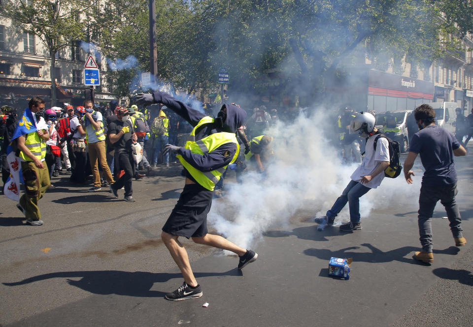 A demonstrator throws back a tear gas canister during a yellow vest demonstration in Paris, Saturday, April 20, 2019. French yellow vest protesters are marching anew to remind the government that rebuilding the fire-ravaged Notre Dame Cathedral isn't the only problem the nation needs to solve. (AP Photo/Michel Euler)