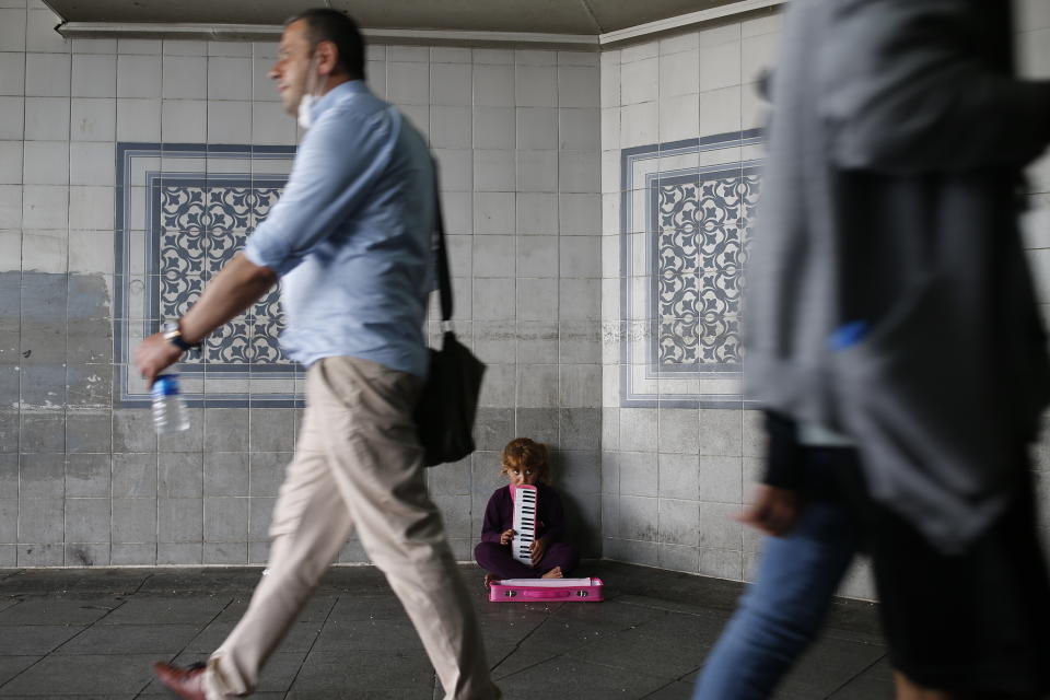 People, some wearing protective masks against the spread of coronavirus, walk by a child playing music for money on an underpass in Istanbul, Thursday, June 18, 2020.Turkish authorities have made the wearing of masks mandatory in Istanbul, Ankara and Bursa to curb the spread of COVID-19 following an uptick in confirmed cases since the reopening of many businesses. (AP Photo/Emrah Gurel)