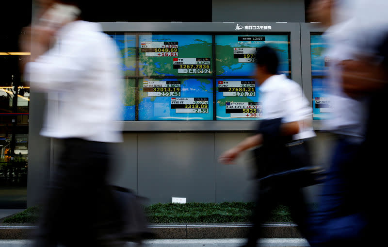 People walk past an electronic board showing Japan's Nikkei average outside a brokerage at a business district in Tokyo, Japan August 9, 2017. REUTERS/Kim Kyung-Hoon