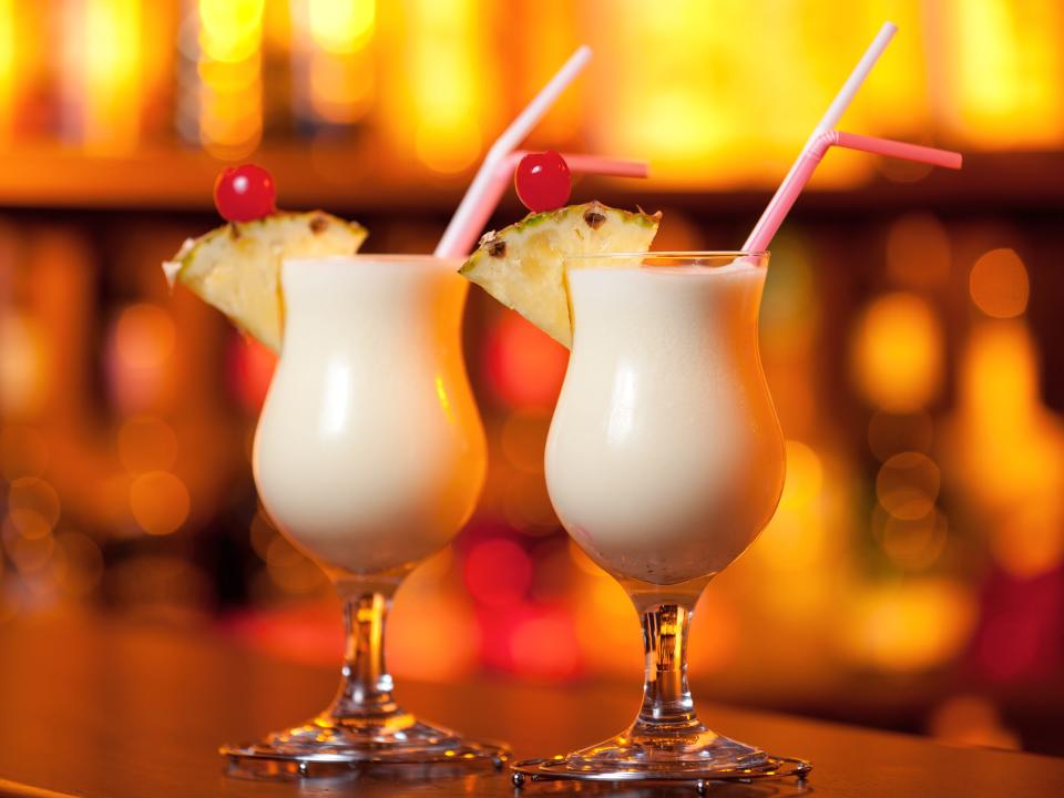 two garnished pina coladas on a bar