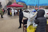 A man wearing a face mask to help protect from the coronavirus walks by medical workers in protective suits taking swab samples for the COVID-19 test from residents in Huaxian county, central China's Henan province on Monday, Jan. 10, 2022. A third Chinese city has locked down its residents because of a COVID-19 outbreak, raising the number confined to their homes in China to about 20 million people. (Chinatopix via AP)