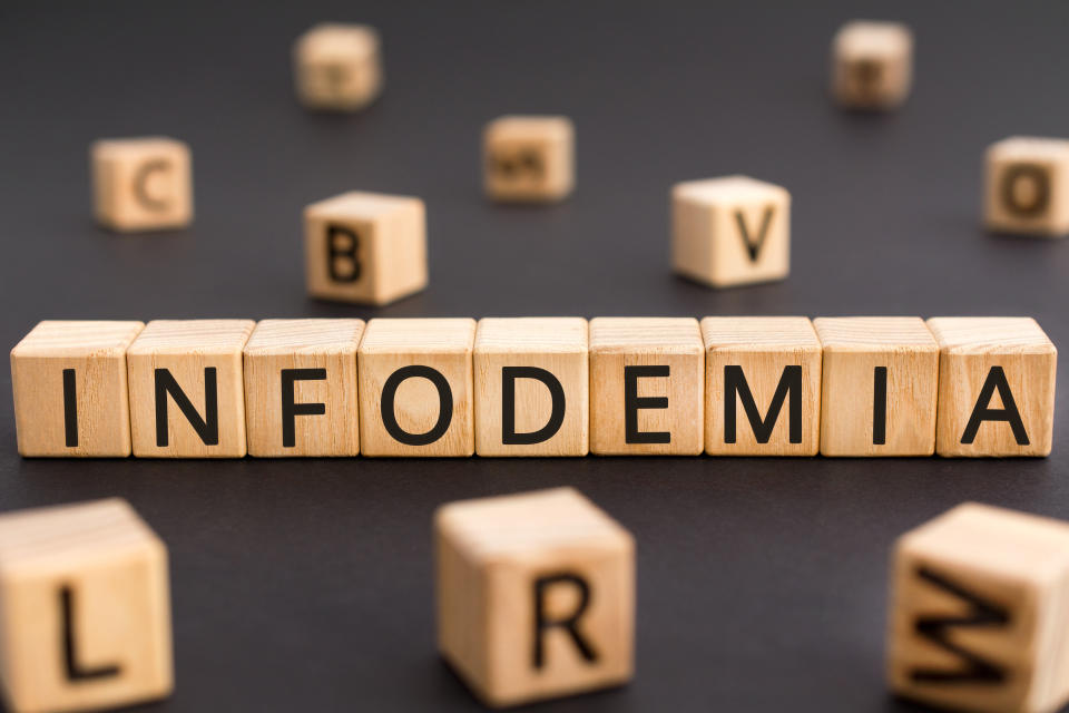 Infodemia - word from wooden blocks with letters, deliberately misinform infodemia concept, random letters around black background