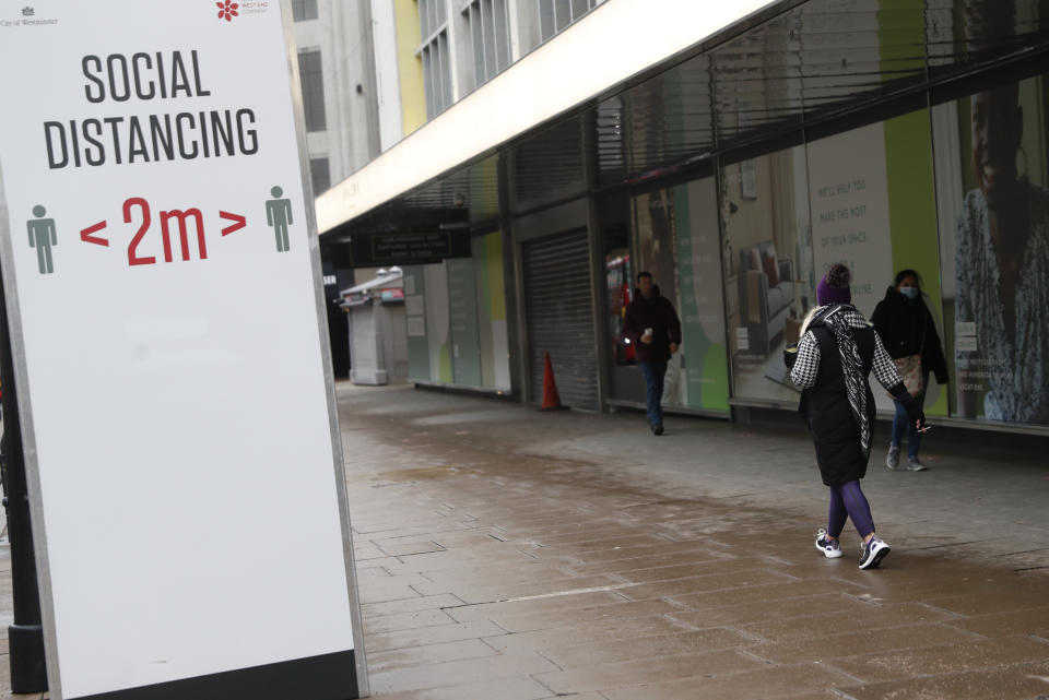 Pedestrians walk past a sign advising them to keep 2 meters apart on Oxford Street in London, Tuesday, Jan. 26, 2021. The U.K. will soon become the fifth country in the world to record 100,000 COVID-19 deaths, after the United States, Brazil, India and Mexico — all of which have much larger populations than Britain's 67 million people. As of Monday, the U.K.'s official coronavirus death toll was 98,531. (AP Photo/Alastair Grant)