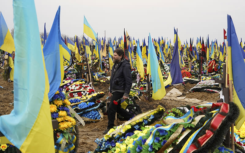 A man carries flowers to lay at the grave of a killed soldier in a city cemetery in Kharkiv, Ukraine