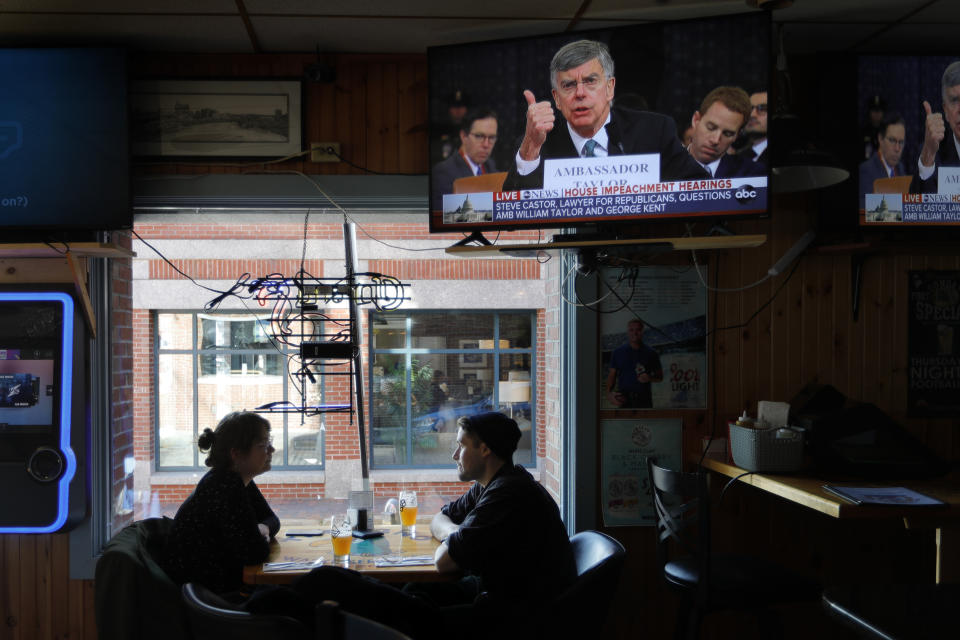 Olivia Tobin and her fiancé, Jordan Ashby, ignore the televised impeachment hearings playing on monitors at the Commercial Street Pub, Wednesday, Nov. 13, 2019, in Portland, Maine. Tobin is an Irish citizen who has a green card to live and work in the U.S. and said she only pays attention to the hearings if it seems likely that the Trump will be held accountable. (AP Photo/Robert F. Bukaty)