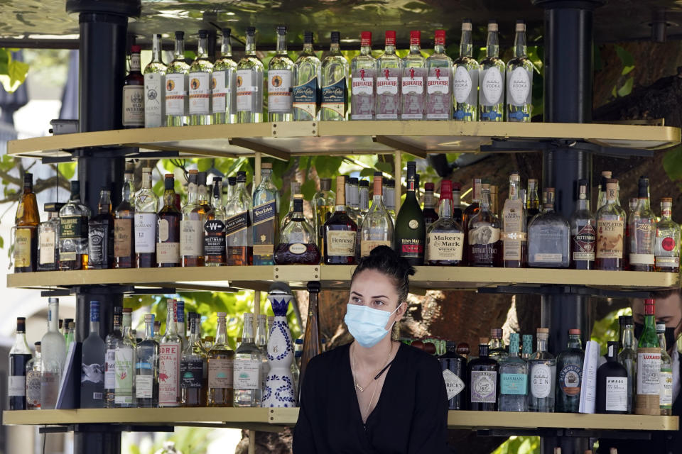 A bartender wears a mask while working at an outdoor bar amid the COVID-19 pandemic Thursday, May 20, 2021, at The Grove in Los Angeles. California regulators will shoot for a mid-June easing of workplace masking and social distancing requirements to conform with a broader state order. They asked to delay a debate Thursday on how quickly they should drop coronavirus safety rules for employees. (AP Photo/Marcio Jose Sanchez)