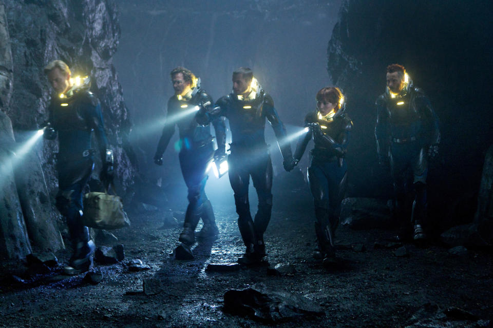 Five people in uniforms walking through a dark cave