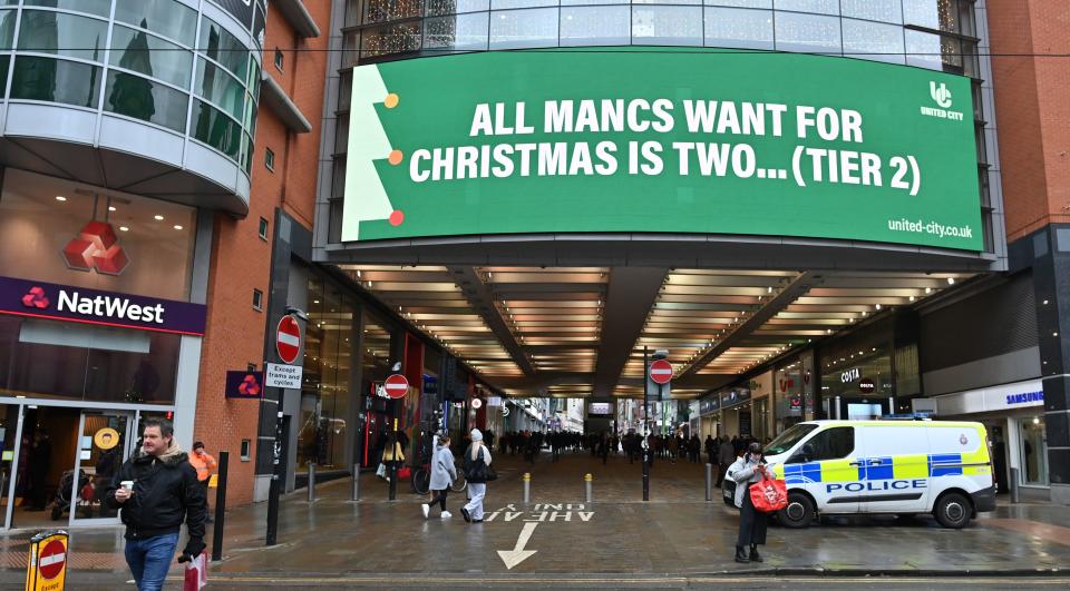 Pedestrians walk beneath a sign reading "All Mancs Want For Christmas Is Two... (Tier2)", referring to manchester's current Tier 3 COVID-19 statues, in Manchester, northern England on December 2, 2020 as England emerges from a month-long lockdown to combat the spread of Covid-19. - England on December 2 exited a month-long lockdown into a new 3-tiered system of curbs with non-essential retail, leisure centres and salons all reopening but with some sectors, including hospitality, seeing tighter restrictions. (Photo by Paul ELLIS / AFP) (Photo by PAUL ELLIS/AFP via Getty Images)