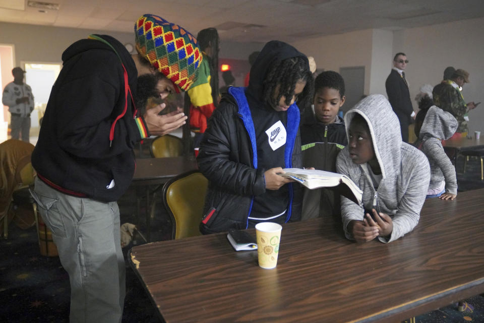 Amaha Sellassie prays as Ras'Micael Inman, 12, Miziah Smith, 9, and Taleia Inman, 10, read the Bible during an event by the Rastafari Coalition marking the 91st anniversary of the coronation of the late Ethiopian Emperor Haile Selassie I in Columbus, Ohio on Tuesday, Nov. 2, 2021. The coronation day event included chanting, traditional nyabinghi drumming and the reading of psalms, which are the core of Rastafari holiday celebrations. (AP Photo/Emily Leshner)