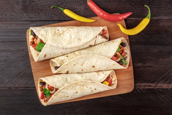 3 burritos on a plate with peppers on the side