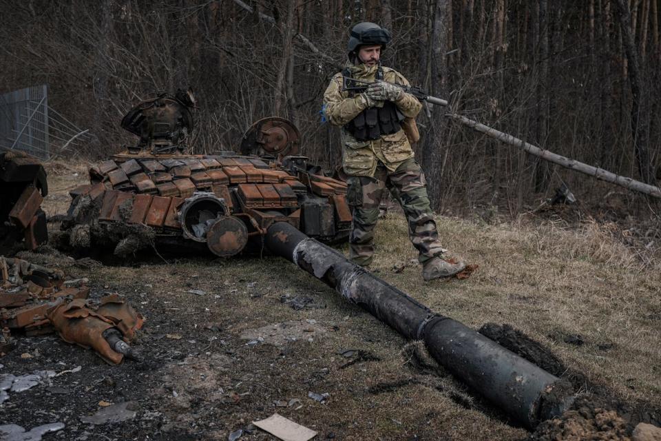 A Ukrainian serviceman walks next to the wreck of a Russian tank in Stoyanka, Ukraine, Sunday, March 27, 2022. Ukrainian President Volodymyr Zelenskyy accused the West of lacking courage as his country fights to stave off Russia's invading troops, making an exasperated plea for fighter jets and tanks to sustain a defense in a conflict that has ground into a war of attrition.