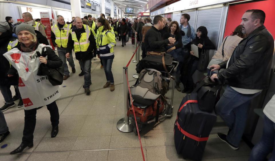 Participants of a strike organized by the German ver.di union walk past travelers queuing in front of a booking change counter at the Tegel airport in Berlin, Germany, Monday, March 13, 2017. The union, representing airport ground staff, has called on its members to go on strike again at Berlin's two airports Tegel and Schoenefeld. (AP Photo/Michael Sohn)