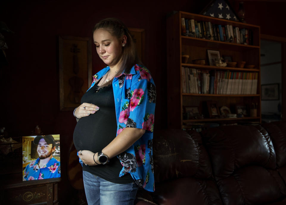 Krista Johnston stands next to a photo of her husband, Sgt. James Johnston, who was killed in Afghanistan in June, while pregnant with their first child, in Trumansburg, N.Y., Saturday, Aug. 31, 2019. As the nation's longest war marks the end of its 18th year, Krista returned to her tiny hometown for two milestones: In one weekend in the local American Legion hall, she joined hundreds to pay tribute to her husband with a 21-gun salute, TAPS and remembrances. A day later, she returned for a baby shower, celebrating the impending birth of their daughter he didn't live to see. (AP Photo/David Goldman)