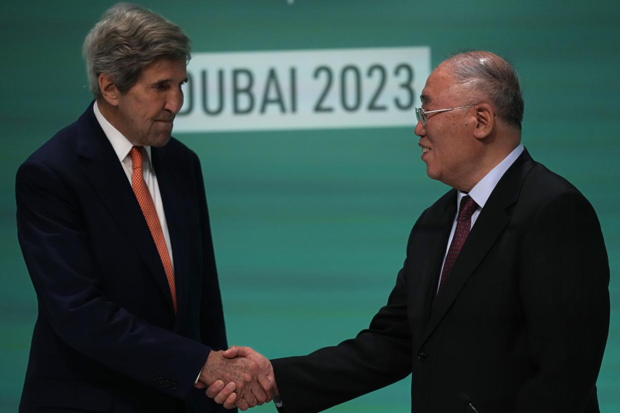 John Kerry and Xie Zhenhua shake hands in front of a sign that reads: Dubai 2023.