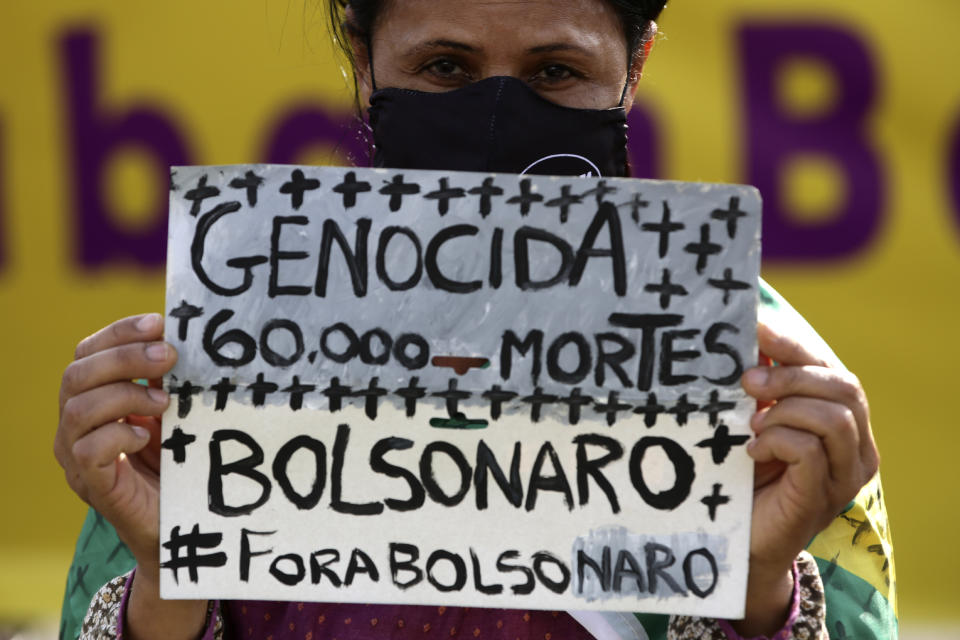 Una activista de los derechos de las mujeres sostiene un cartel en portugués con el mensaje "Genocida 60.000 muertes. Fuera Bolsonaro", durante una protesta contra la gestión del gobierno de la pandemia del coronavirus y la brutalidad policial contra los negros, ante el Congreso Nacional en Brasilia, Brasil, el jueves 2 de julio de 2020. (AP Foto/Eraldo Peres)