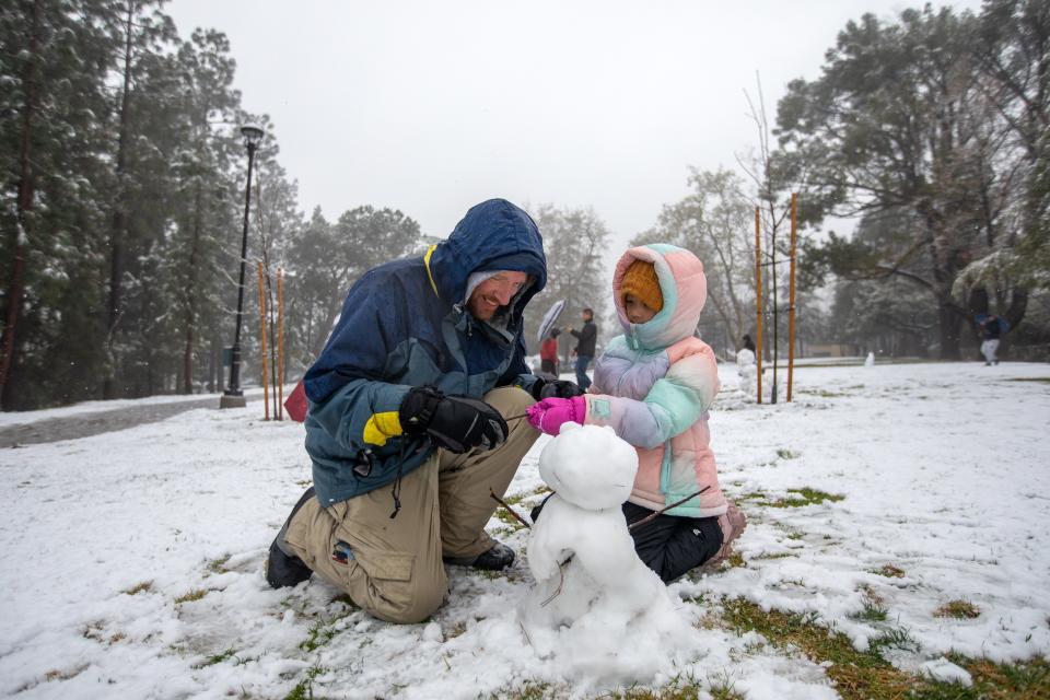 father and daughter in winter gear build small snowman after california blizzard