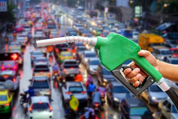 Someone holding a gas pump, with a city street crowded with car traffic in the background.