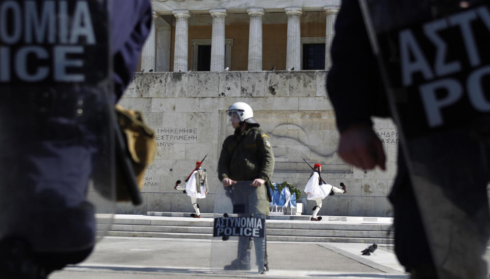 Greek presidential guard, known as Evzones, takes part in a changing of the guard ceremony at the Tomb of the Unknown Soldier, in front of a riot police who secure the Greek parliament, in central Athens as few hundred protesters gathered to protest against austerity measures during an anti-government rally on Sunday, Feb. 19, 2012.(AP Photo/Petros Giannakouris)