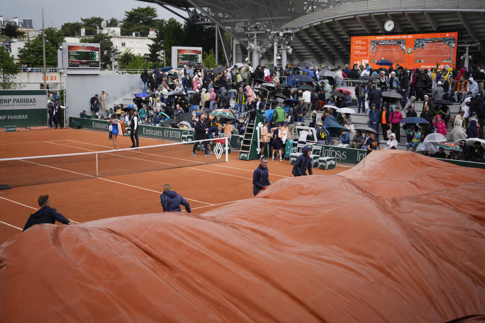 Stadium workers cover the court due to the rain during the French Open tennis tournament at the Roland Garros stadium in Paris, Thursday, May 30, 2024. (AP Photo/Thibault Camus)