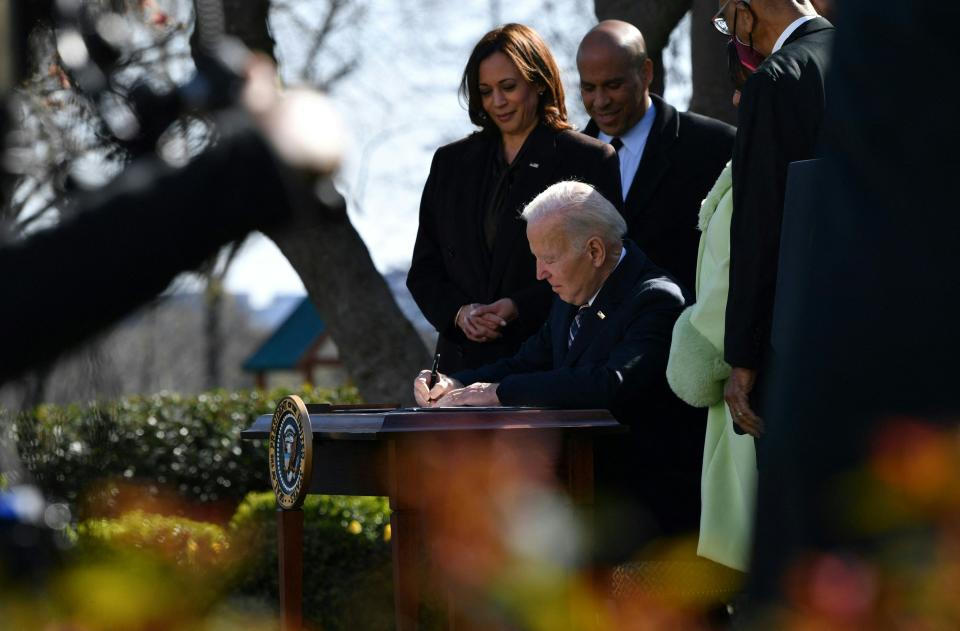 Joe Biden sits at a desk outside and signs a bill into law.