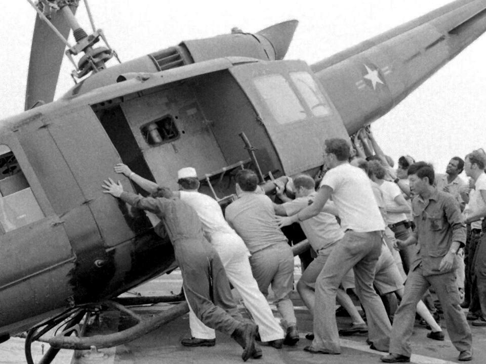 Image of US Navy personnel pushing an army helicopter off the deck of a US Navy carrier to make room for more refugee flights. Fall of Saigon, 29 April 1975