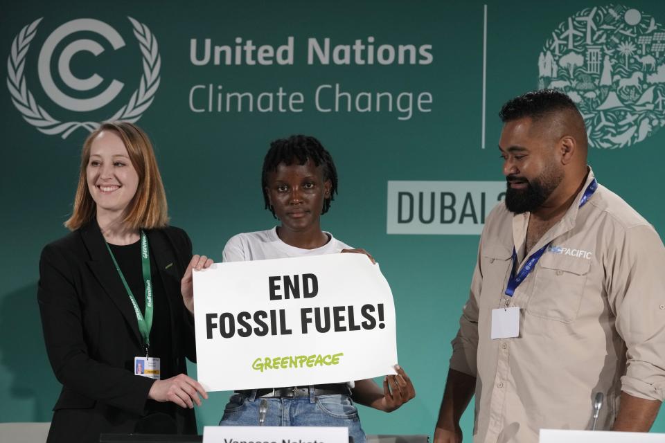 Vanessa Nakate, center, poses for a photo with Lisa Goeldner and Joseph Sikulu with a sign that reads "end fossil fuels" at the COP28 U.N. Climate Summit, Tuesday, Dec. 5, 2023, in Dubai, United Arab Emirates. (AP Photo/Peter Dejong)