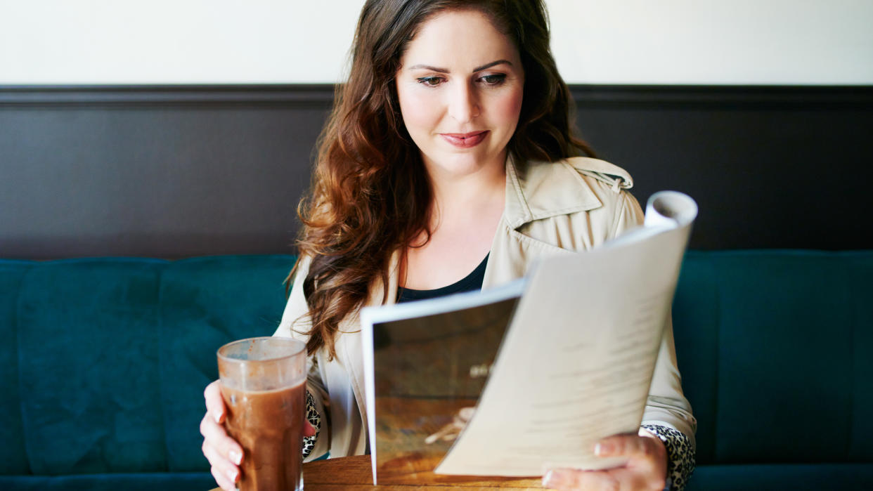 Shot of a young woman reading a magazine in a cafe.